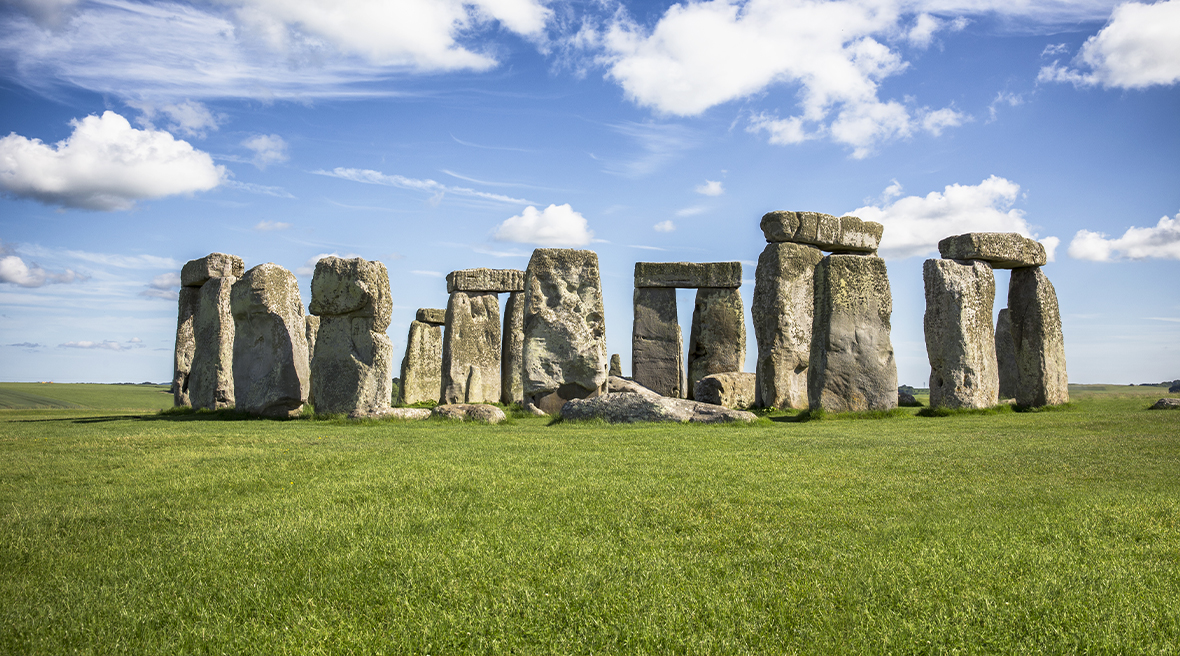 circle of large stones called Stonehenge on green grass with blue sunny skies above